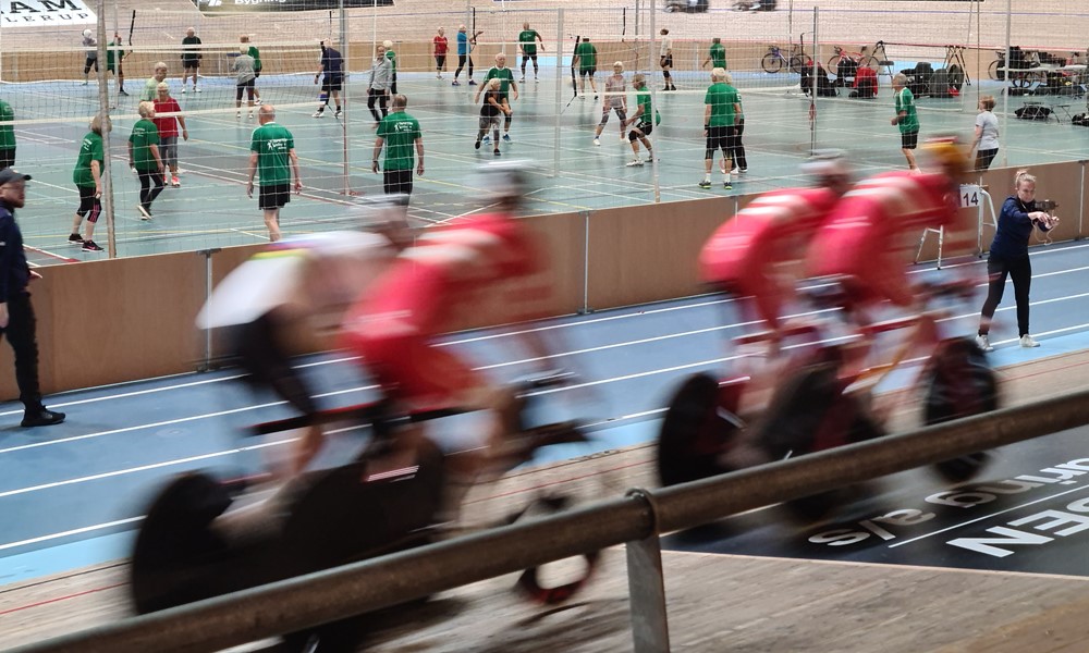 Cykelryttere på cykler og pensionister spiller volleybold